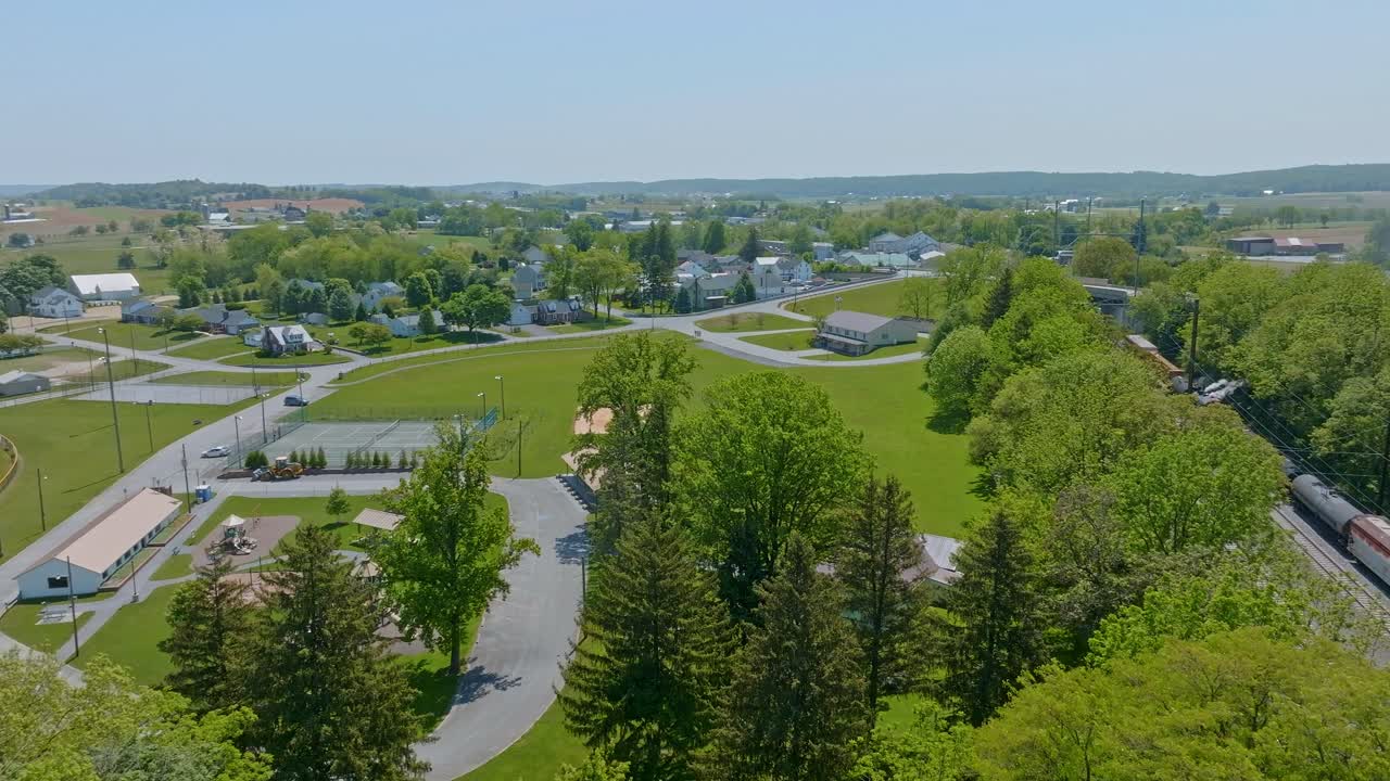 This captivating visual presents a stunning view of lush green fields and a quaint village under clear skies during spring. The area is filled with trees, homes, and well-maintained roads.