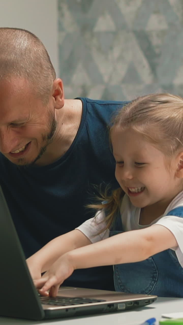 Slow motion: laughing bald father and pretty little girl with plaits have fun doing homework on computer at table in room at quarantine time