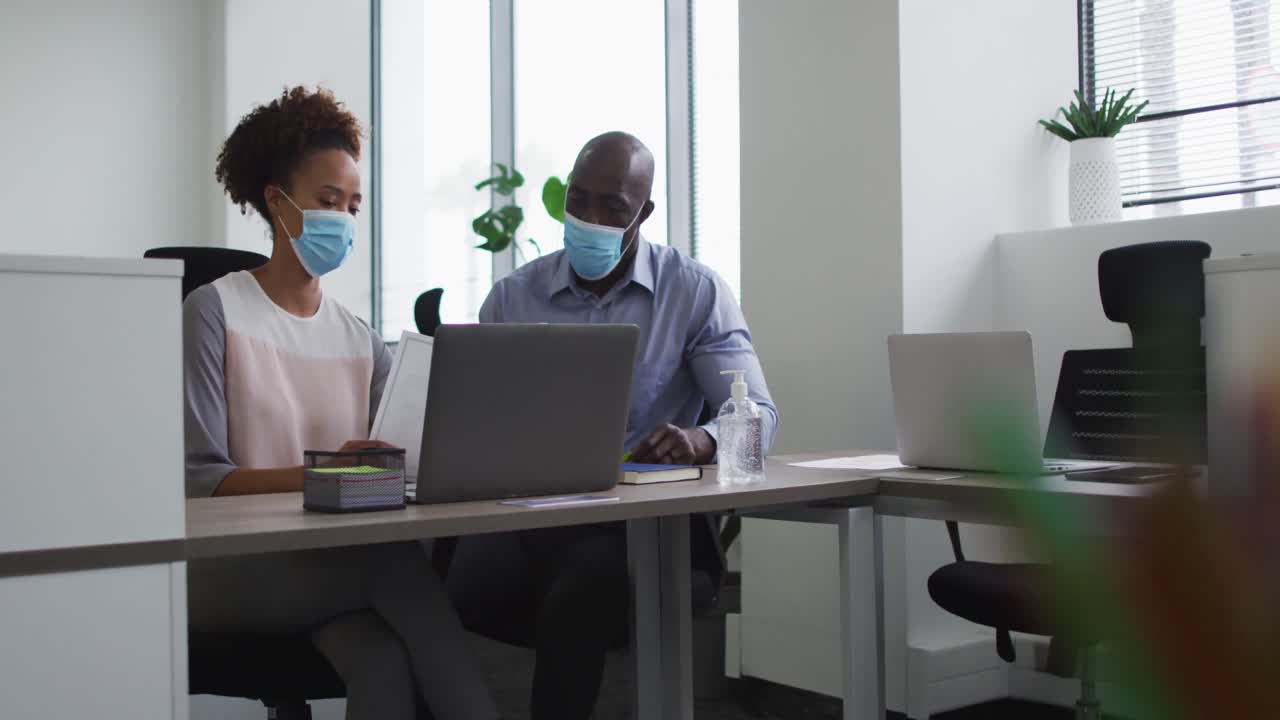 Diverse businessman and businesswoman in face masks discussing in office