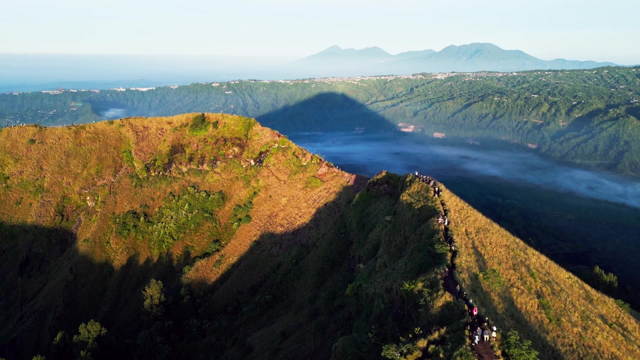 Escursione sul vulcano lungo un'aspra cresta montuosa con viaggiatori che esplorano gli altipiani di Kintamani Bali sopra la nebbia fluttuante e la luce dorata dell'alba su un paesaggio montano tropicale - Ripresa aerea con drone in avvicinamento