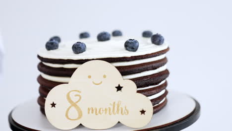 home-made chocolate cake with whipped cream and blueberries. a wooden table with eight months sign on. close up. white backdrop.