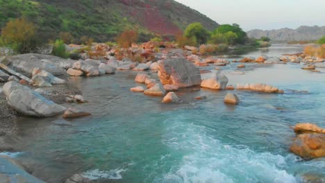 Low-Flying-Aerial-Along-Flowing-River-Above-Rocks-In-Balochistan