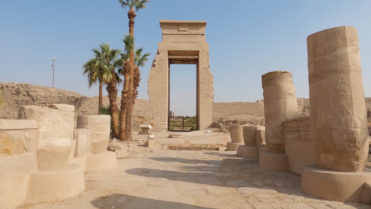 vista mirando a través de pilares de arenisca medio rotos hacia la ruina de una gran puerta en el complejo del templo de karnak en egipto