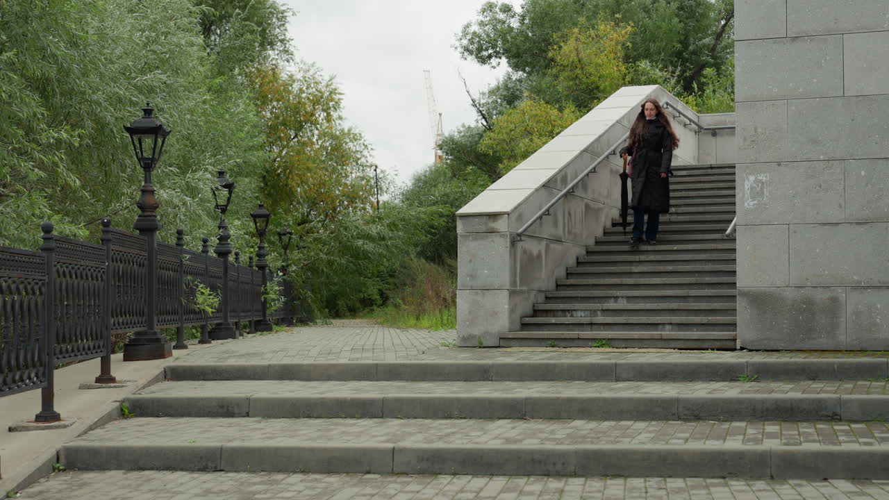 stone steps in park pedestrian walking down staircase, featuring iron railing and vintage lampposts, overcast sky and dense green foliage, slow cinematic broll capturing commuter descent