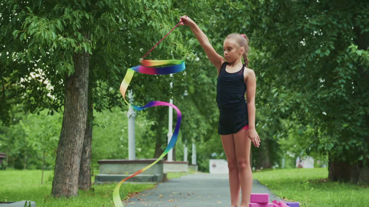 A Young Girl Shows Impressive Rhythm and Grace While Performing with Colorful Ribbons in a Lush Green Park Setting, Captivating the Moment of Joy and Expression