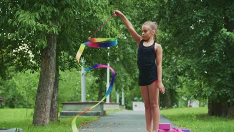 a young girl shows impressive rhythm and grace while performing with colorful ribbons in a lush green park setting, captivating the moment of joy and expression