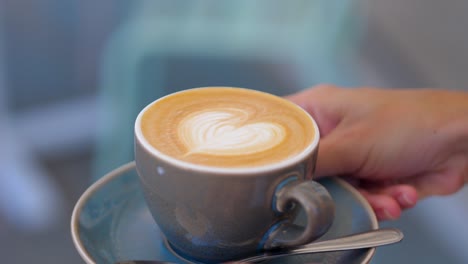 side view of faceless waiter serving cappuccino with heart shape inside cafe natural light