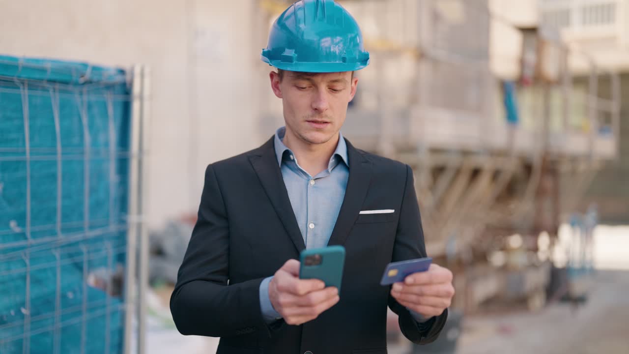 joven arquitecto caucásico usando teléfono inteligente y tarjeta de crédito en la calle