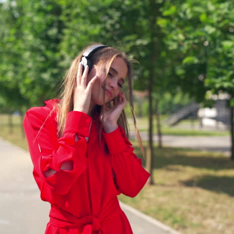 lovely girl listening to music outdoors. beautiful young woman with black headphones standing in the street and enjoys music on the city background in summer.