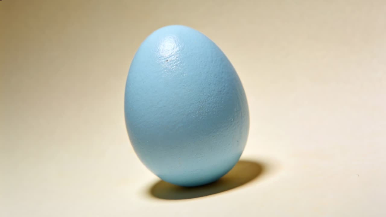 Rotating from left tilt, light-blue egg straightening on beige tabletop, with shadow centering