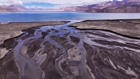 melting icy water creating abstract curvy stream as it meanders over glacial flat stony lands to mountain lake. drone fly reveal