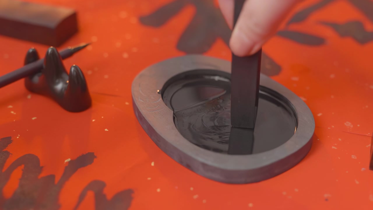 Le mani dell'artista calligrafo macinano l'inchiostro in stick su una pietra d'inchiostro, pronto a scrivere calligrafia cinese tradizionale su carta cremisi; abili pennellate creano caratteri eleganti con una scrittura che esprime saggezza.