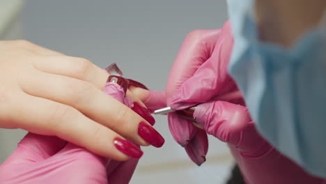 close up of nail technician in pink gloves carefully applying red nail polish using tiny brush to refine edge of nail, while her hair partially obscures view, showing focus and precision in detailing