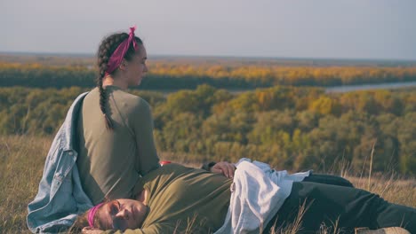 chica con bebida y compañero descansa después de una caminata en la hierba de otoño