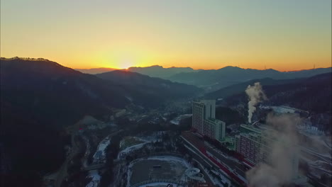 Sun-rises-above-mountain-ridge-near-cityscape-in-winter-season,-aerial-view