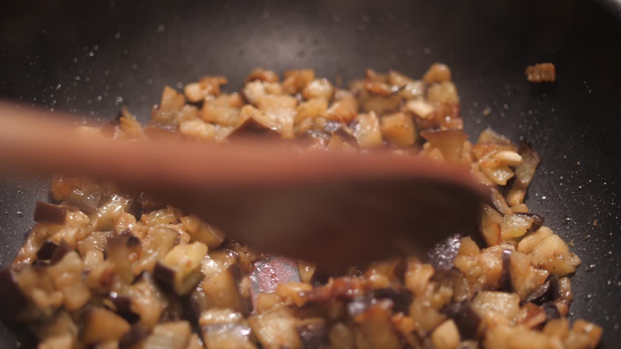 revolviendo el plato de berenjena con una cuchara de madera cortada en cubos en una sartén