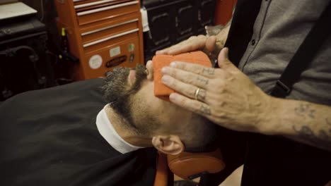 barbero aplicando una toalla caliente en la cara del cliente en la barbería - de cerca