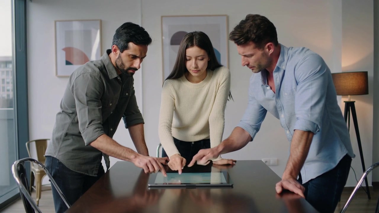 Tre colleghi che indicano e toccano il tablet sul tavolo in sala riunioni, collaborando in abbigliamento business casual.
