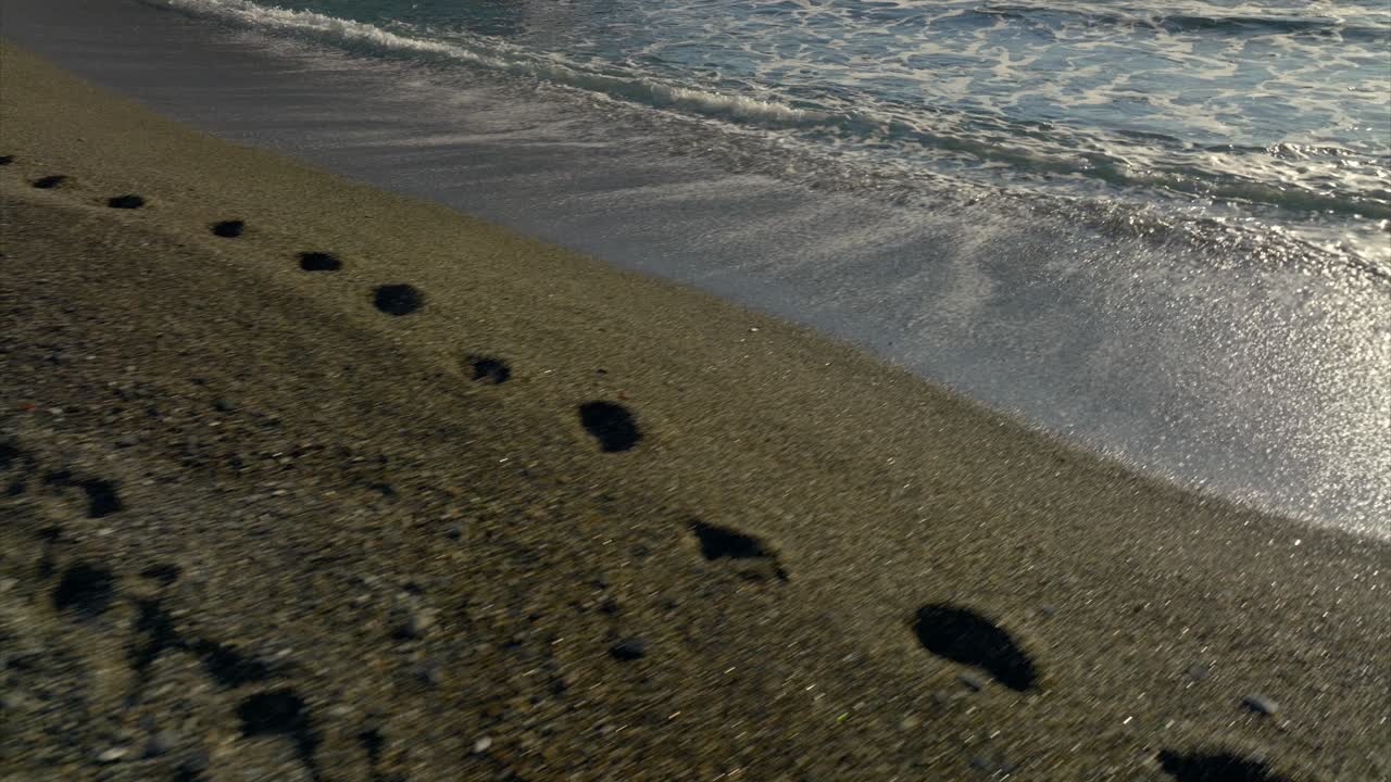 camminare all'indietro sulla spiaggia sabbiosa con le onde del mare che si infrangono sulla riva e le impronte sulla sabbia al tramonto