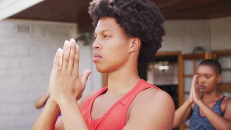 african american man practicing yoga with group of diverse friends in backyard