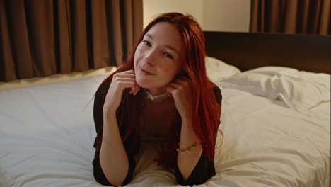 beautiful red haired woman lies in bed and plays with her long hair