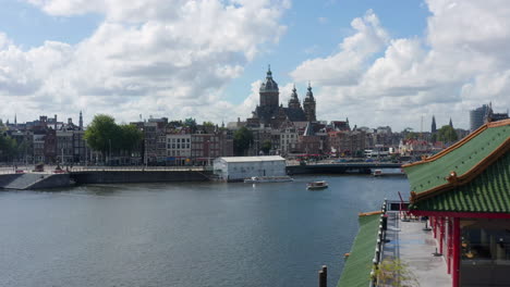 Riverside-and-Basilica-of-Saint-Nicholas,-Amsterdam-with-Asian-Building-in-foreground,-Aerial-forward