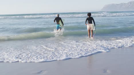 Happy-african-american-couple-running-with-surfboards-on-sunny-beach