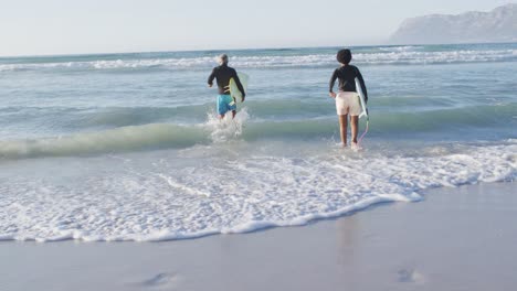 happy african american couple running with surfboards on sunny beach