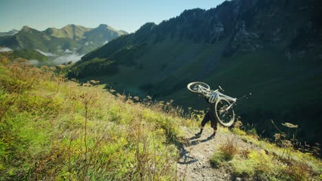 a mountain biker is carrying his bike up an alpine trail in autumn