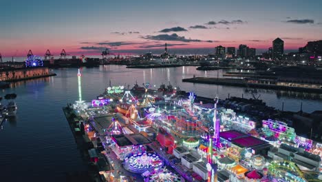 Drone-view-of-illuminated-Winter-Park-Genova-on-harbor-waterfront,-twilight-sky