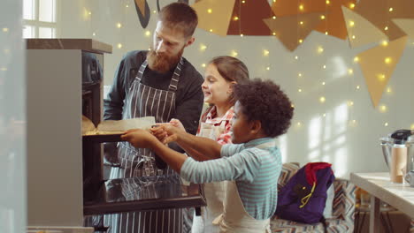 Niños-Alegres-Ayudando-Al-Chef-A-Poner-Una-Bandeja-Para-Hornear-En-El-Horno-Durante-La-Clase-De-Cocina