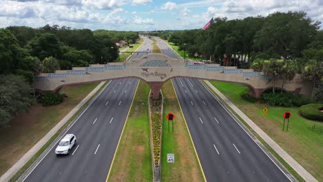 the villages sign on a decorative overpass spans a wide boulevard near spanish springs in florida. palm trees and greenery line the road, with light traffic passing underneath. aerial.