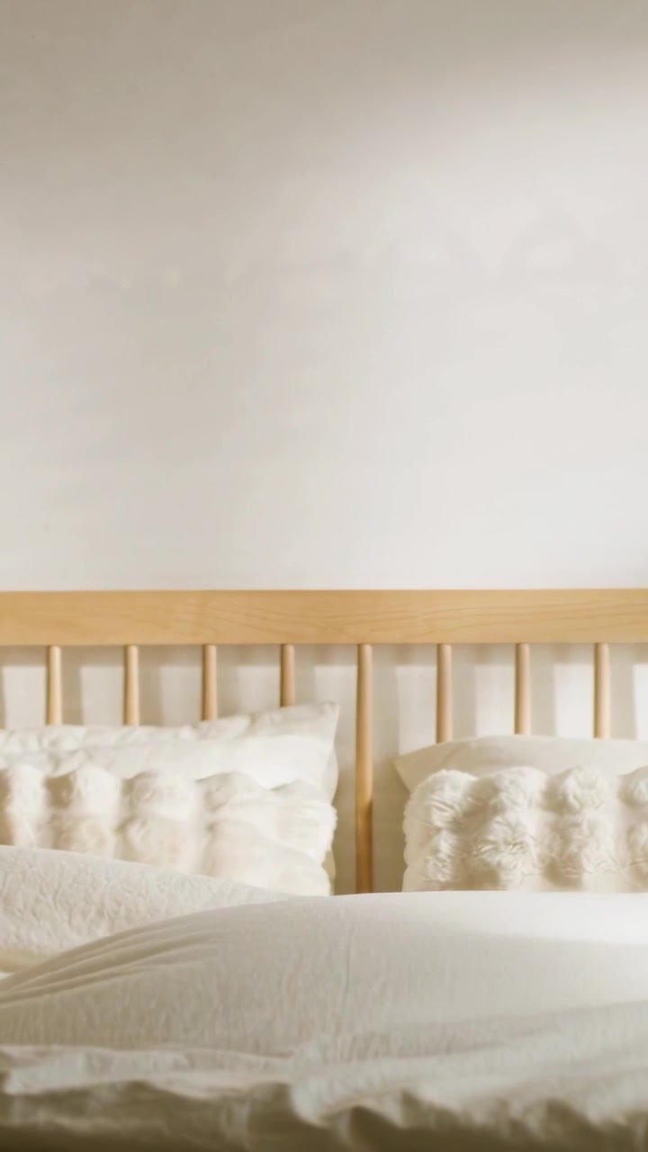 Vertical video: Tossing duvet offscreen at home, smoothing bed and revealing headboard and pillows