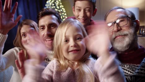 pov f joyful lovely caucasian family with kids gathered together in cozy room with glowing xmas tree and video chatting online sending holiday greetings to friends happy holidays concept