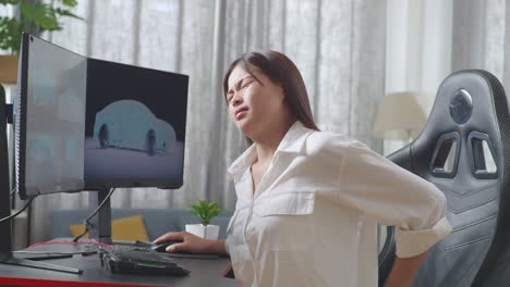 side view of asian female automotive designer having a backache while working on 3d model of ev car on the desktop computers in the studio