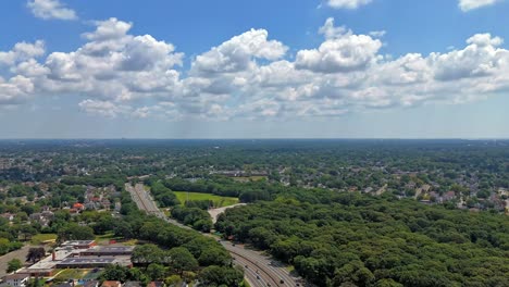 an aerial time lapse over southern state parkway on long island during a sunny day. flying over green trees in the suburban neighborhood. the camera dolly out and tilt down over the landscape