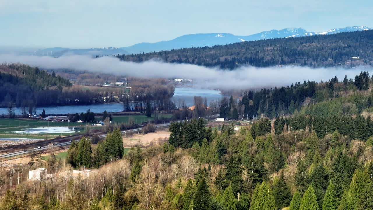 Mission, British Columbia, Canada - A Blanket of Low-lying Fog Drifts Gently Over the River, Nestled Between Forested Hills and Snow-capped Mountains - Aerial Drone Shot