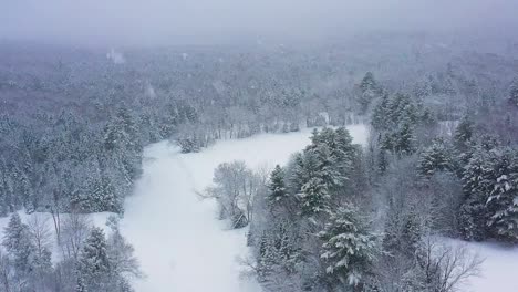 Flying-through-a-blizzard-above-a-frozen-river-curving-through-a-forest-SLOW-MOTION-AERIAL
