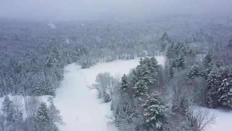 flying through a blizzard above a frozen river curving through a forest slow motion aerial