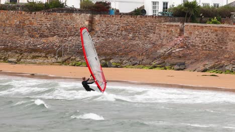 windsurfer navigating waves near a stone wall