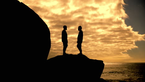 silhouetted men on a cliff at sunset