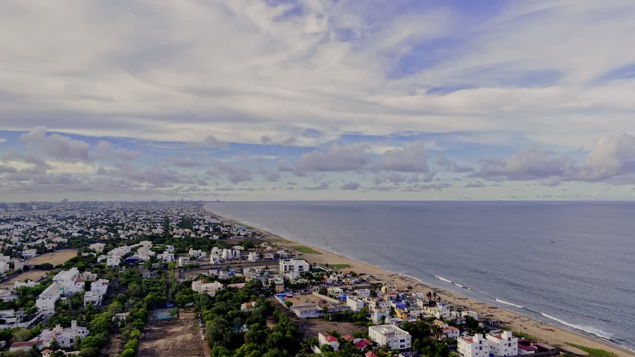 Drone footage of a city located at coastal area of sea with waves lapping into shore. Day view.