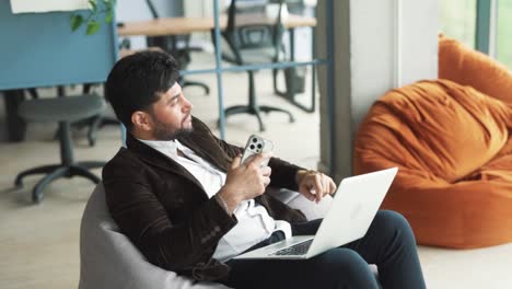 portrait-of-a-handsome,-stylish-young-man-of-Arab-appearance-sitting-in-a-modern-office-of-a-business-center,-receiving-joyful-news-about-a-victory,-feeling-happy-and-dreaming