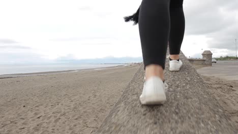 low angle follow pov of girl having fun walking on narrow beach wall