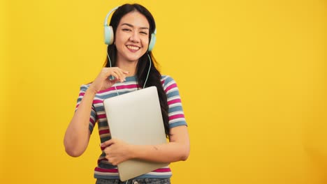feliz joven asiática atractiva bailando aislada en fondo amarillo. alegre chica bonita feliz con tableta portátil música en línea sonriendo y moviendo el cuerpo seguir la música con positivo.