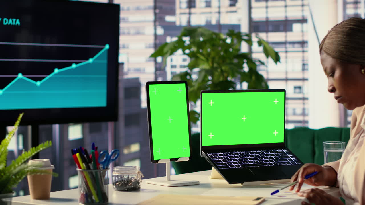 Office setup with laptop and tablet displaying a green screen