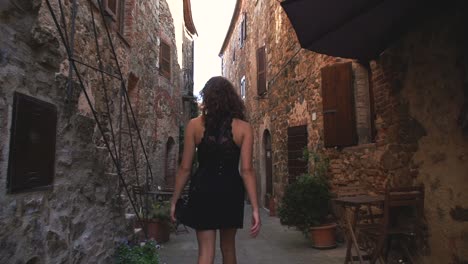 a young brunette woman in a black dress is walking through a little medieval italian village