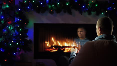 a man with a glass of spirits sits by the fireplace decorated for christmas