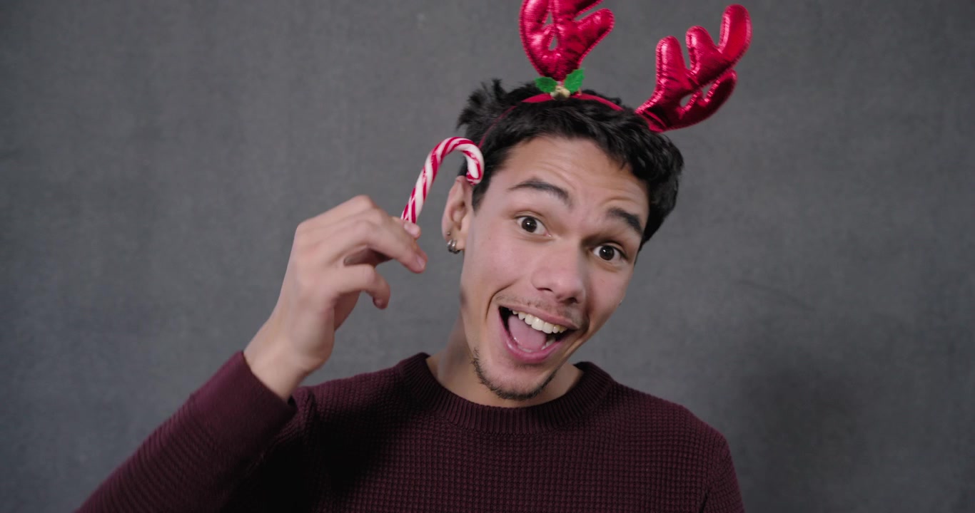 African American adult male holding candy cane near face, tapping antler headband, celebrating
