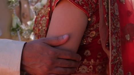 the hindu groom gently caressing his bride's arms as a gesture of affection during their wedding ceremony - close up